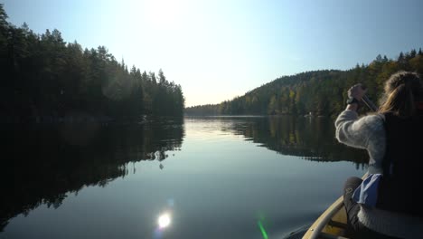 woman paddling canoe boat on beautiful autumn lake, rear view