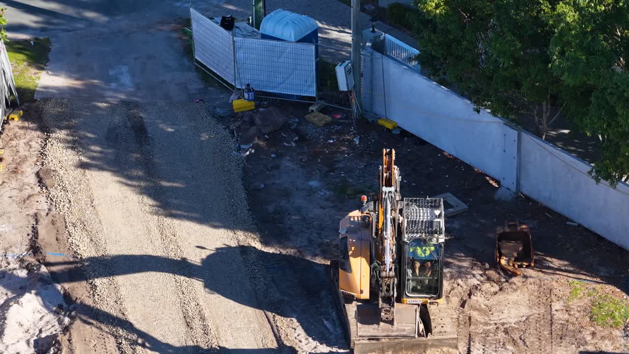 Excavator distributes gravel along driveway, aerial view, bright daylight, steady camera, construction environment