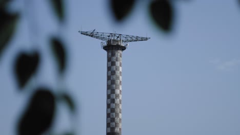 Feste-Aufnahme-Eines-Fallschirmsprungturms-Mit-Blättern-Im-Vordergrund-Und-Einem-Klaren-Blauen-Himmel-Im-Hintergrund