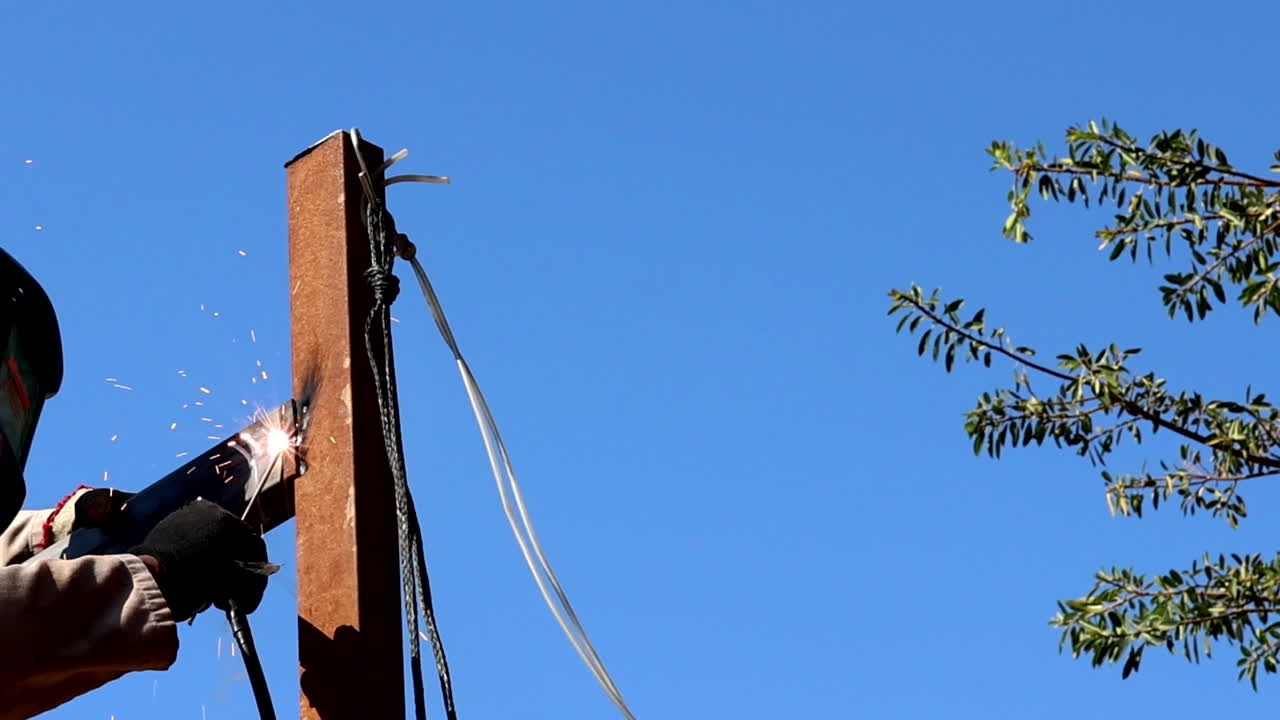 Tradesman welding steel support poles outdoors ensuring safety standards