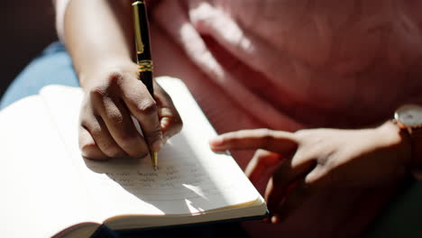 primer plano de una mujer afroamericana escribiendo en un cuaderno en casa