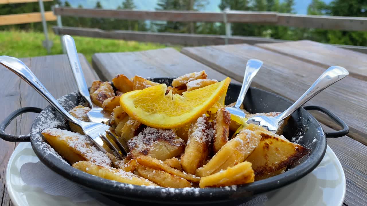 plato de postre tradicional austriaco kaiserschmarren con una hermosa vista de las montañas en tirol austria, dulce y esponjoso panqueque triturado con una naranja en serfaus fiss ladis, verano, tiro de 4k