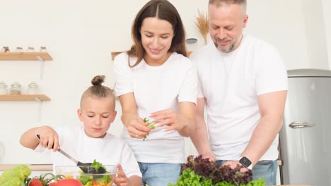 family couple with children preparing healthy food in their kitchen vegan food family couple with children preparing healthy food in their kitchen preparation of salad from fresh vegetables