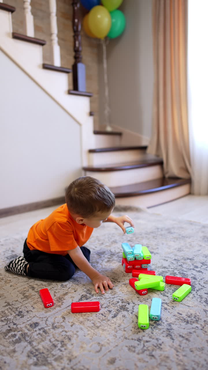 Calm baby boy sitting on the floor builds a tower. Happy child playing with toys at home. Vertical video.