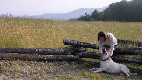 Woman-plays-with-white-lab-along-fence-line-with-mountain-backdrop