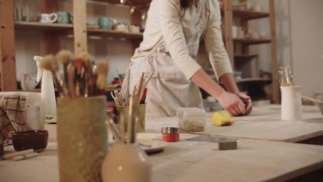 young woman potter working in art studio - kneads clay on the table