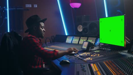 elegante productor de audio que trabaja en un estudio de grabación de música, utiliza una pc de pantalla verde, un ecualizador de placa de mezcla y un escritorio de control para crear nuevas canciones y canciones de éxito. músico artista negro creativo. retrato de vista lateral