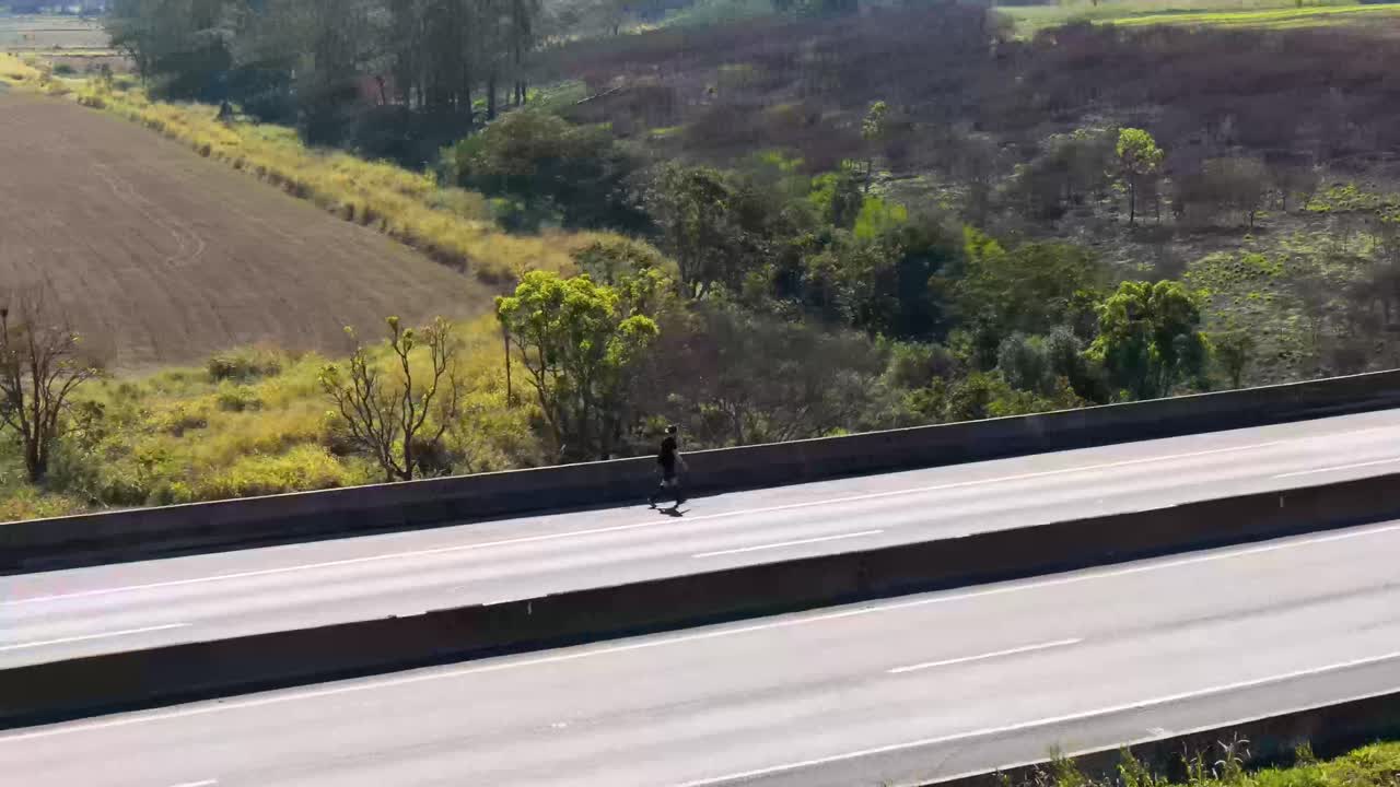 Pedestrian walking along a highway as vehicles pass by with a rural backdrop.