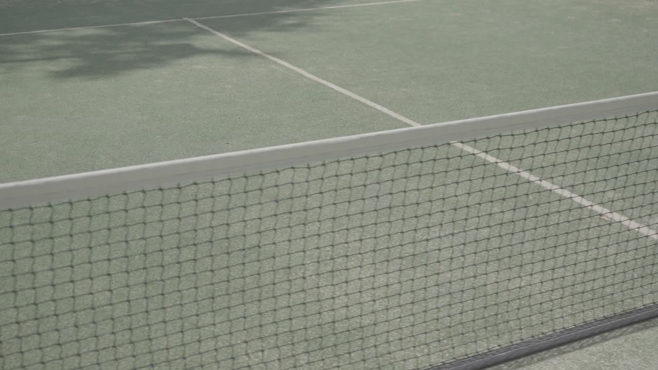 Slow establishing shot of a paddle courts net projecting shadows in the sun