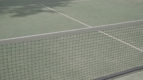 slow establishing shot of a paddle courts net projecting shadows in the sun
