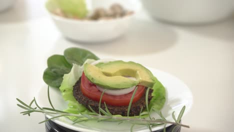 Vegan-raw-burger-garnished-with-thyme-avocado-slices-spinach-leaves-onions-and-butter-lettuce-rotating-on-a-plate