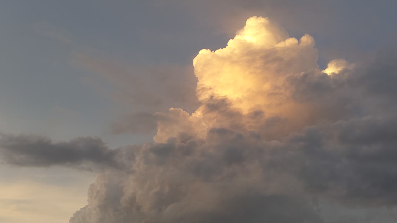 con una nube de escenario de cúmulo elevada iluminada por la puesta de sol que crece y se forma nubes más altas y oscuras que pasan frente al cúmulo en ascenso a medida que el color de la puesta de sol se desvanece de la nube