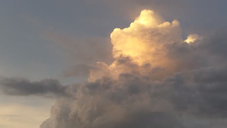 with a sunset illuminated towering cumulus stage cloud growing and forming taller, darker clouds pass in front of the rising cumulus as the sunset color fades from the cloud