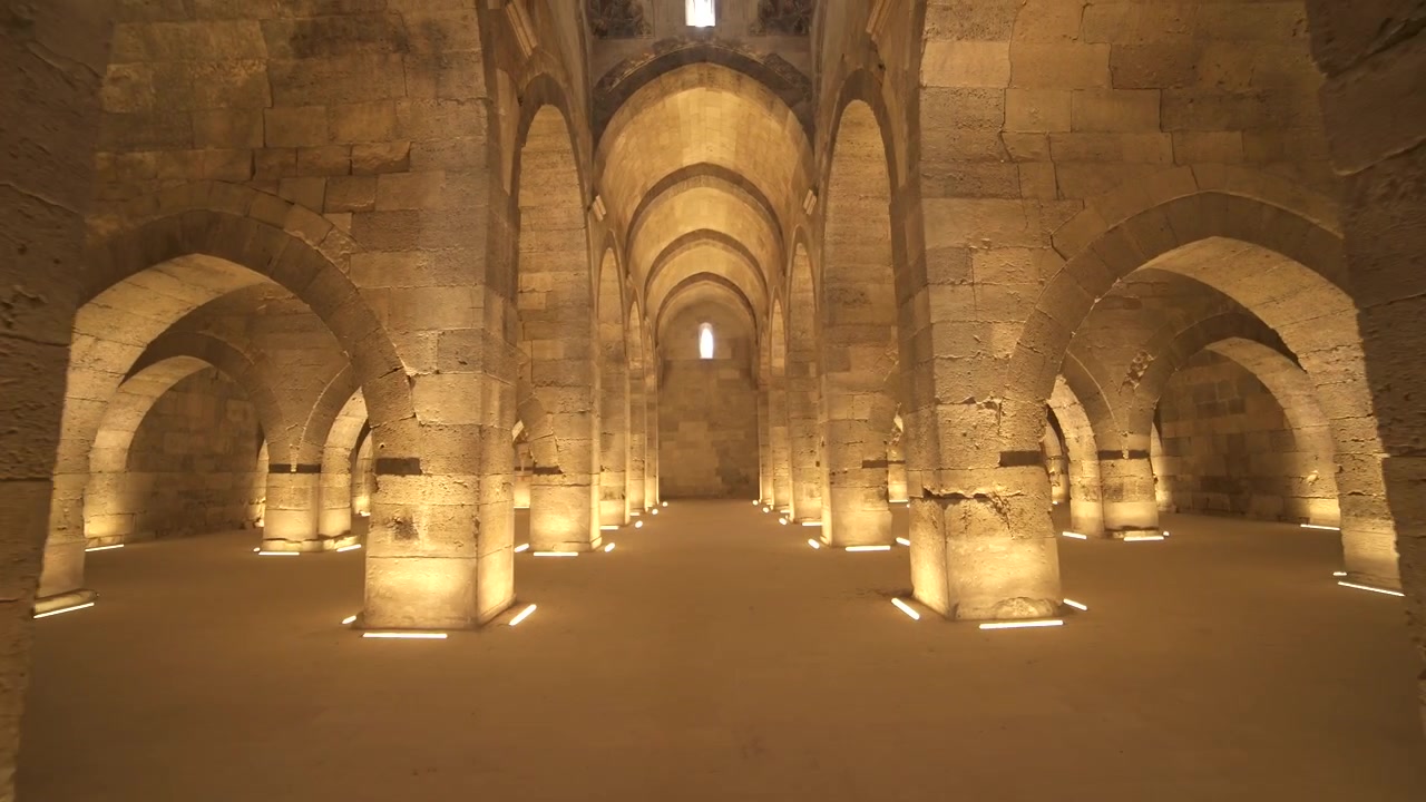Vista Interior de Antigo Salão Abobadado de Pedra com Colunas Iluminadas.