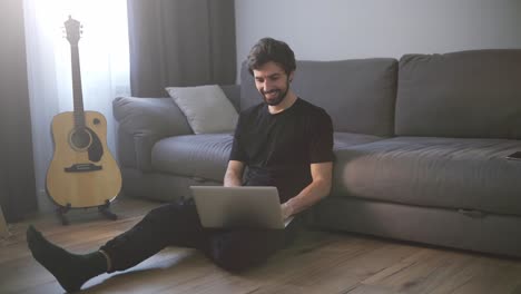 Lächelnder-Mann,-Der-Auf-Dem-Boden-Sitzt,-Während-Er-Zu-Hause-Mit-Einem-Laptop-Videoanrufe-Tätigt