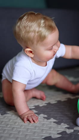adorable blond caucasian blue-eyed baby sitting on the floor. close up portrait of a cute child wearing white bodysuit. vertical video.