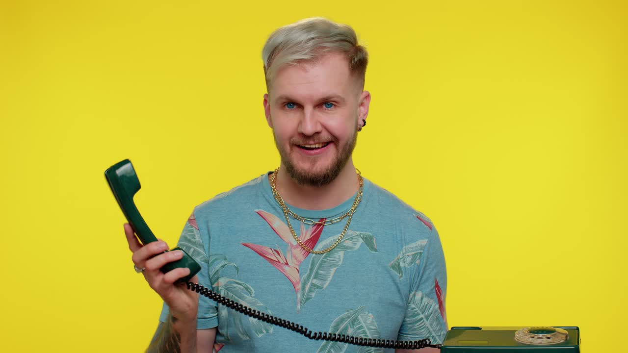 un joven loco y sincero hablando por teléfono vintage de los años 80, engañando, haciendo caras divertidas y tontas