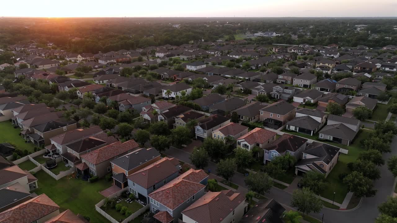 Riprese aeree di una città americana in Florida, con una splendida architettura residenziale circondata da una vegetazione lussureggiante. Il tramonto proietta un caldo bagliore, evidenziando le case uniche e lo stile di vita rilassato
