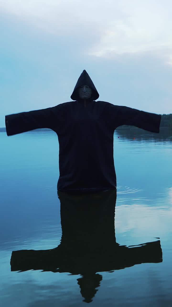 Evil witch in black cloak with hood in the river. Halloween costume. Vertical video