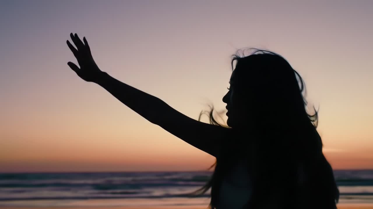 A person stands at the beach during sunset, their silhouette highlighted against the vibrant evening sky. Waves gently crash as they wave their hand, embracing the beauty of nature.