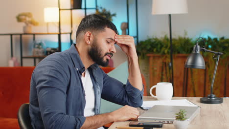 tired exhausted busy multitasking indian businessman working on laptop feels sad boredom at office