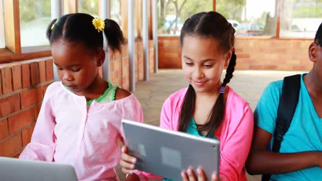 Gruppe-Von-Schulkindern,-Die-Auf-Dem-Campus-Ein-Digitales-Tablet-Und-Einen-Laptop-Nutzen