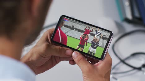 Composite-of-male-doctor-watching-rugby-match-on-smartphone