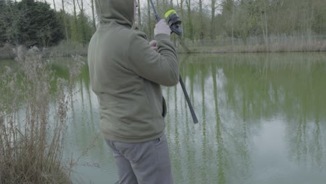 a fisherman reeling a fishing rod at a carp pond