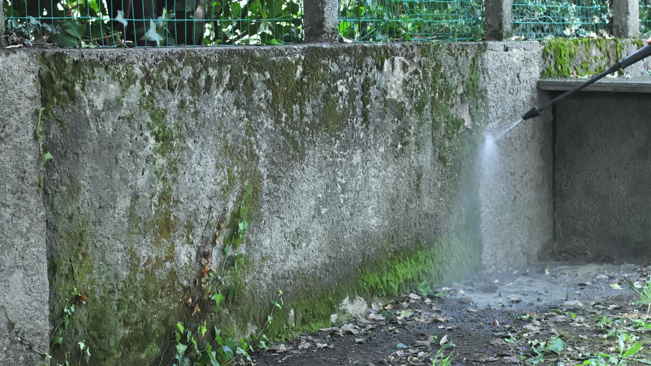 Young strong Caucasian man power washing, spraying and cleaning concrete scarp