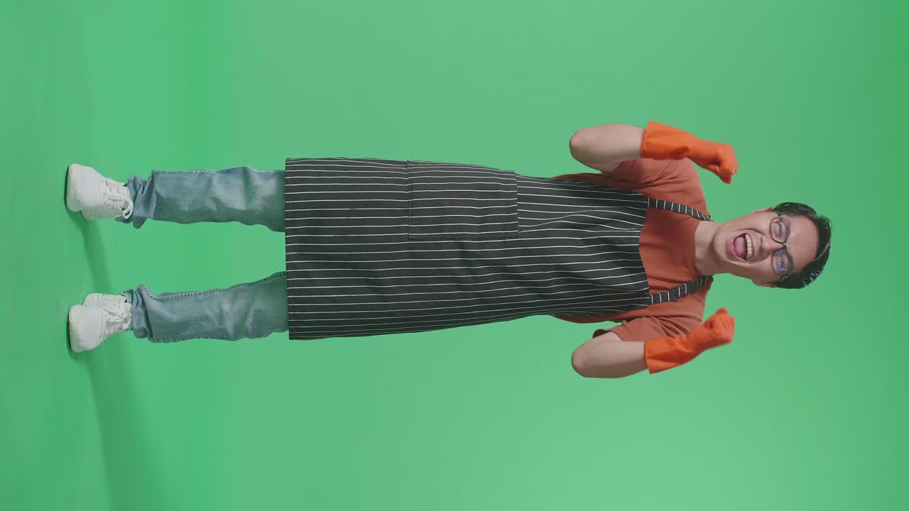 Full Body Of Happy Asian Male Housekeeper With An Apron Celebrating While Standing In The Green Screen Studio