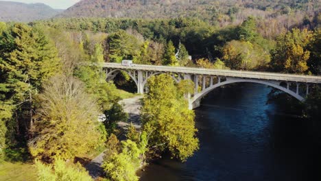 toma aérea de un puente sobre el río housatonic que pasa con la vista de una camioneta blanca que pasa por un terreno montañoso en el condado de litchfield, connecticut, estados unidos