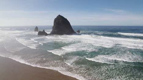 blue water and crashing waves surround haystack rock at cannon beach