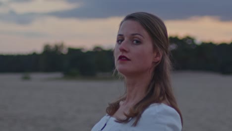 attractive woman standing in sand dunes at golden hour and turning her head towards camera