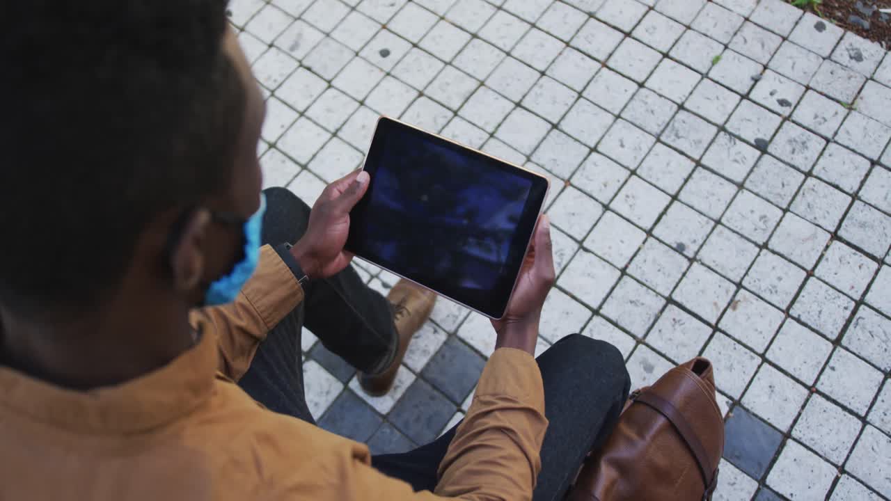 African american businessman wearing face mask using tablet in sitting in street