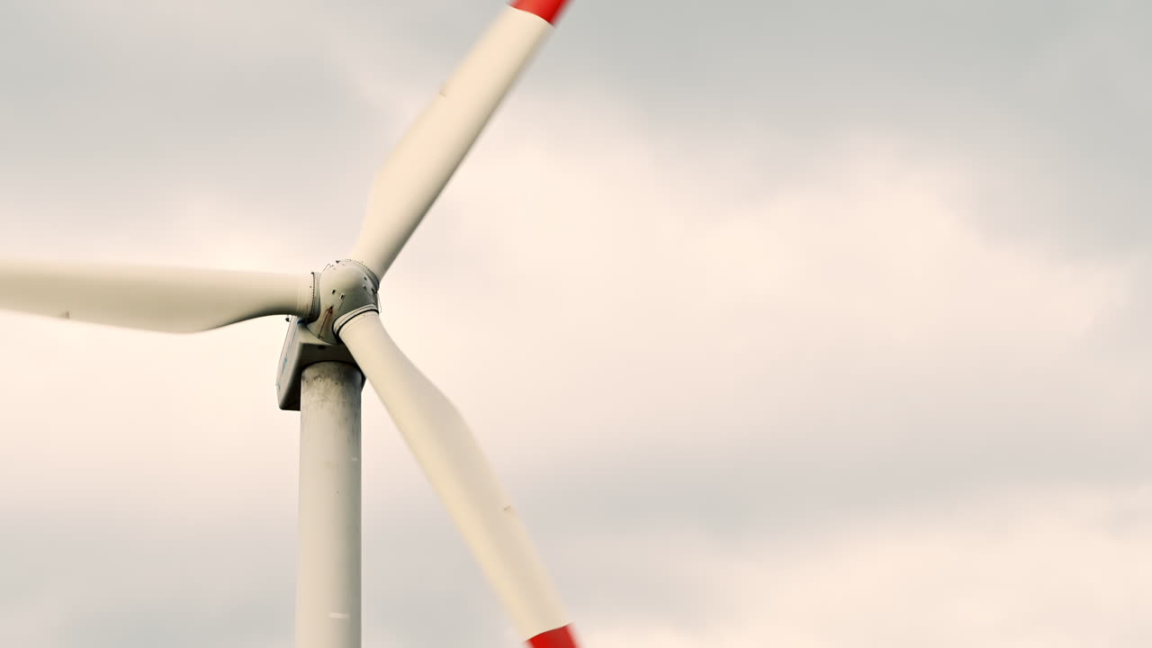 A single wind turbine turning slowly above a field with two trees and a cloudy sky