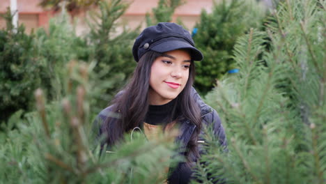 a hispanic woman shopping for a seasonal holiday christmas tree decoration on a lot with many species of festive trees