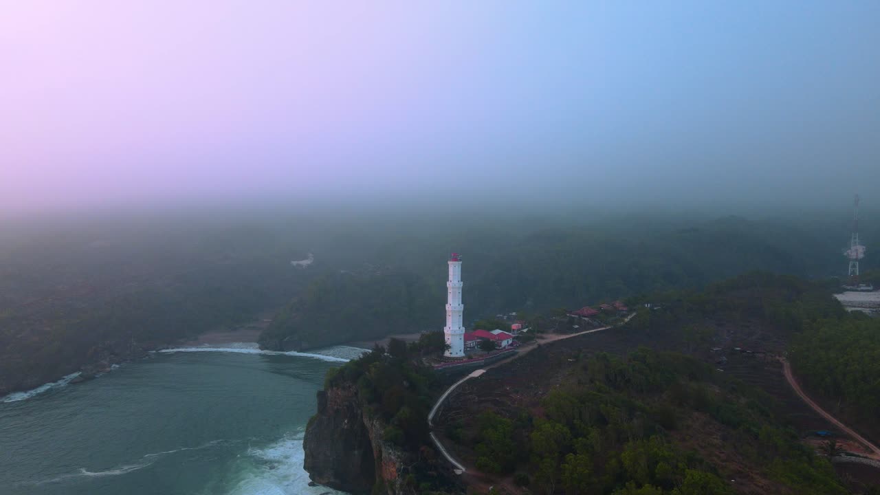 vista aérea del faro blanco en la costa montañosa en el cielo de la noche nebuloso - playa de baron, yogyakarta, indonesia