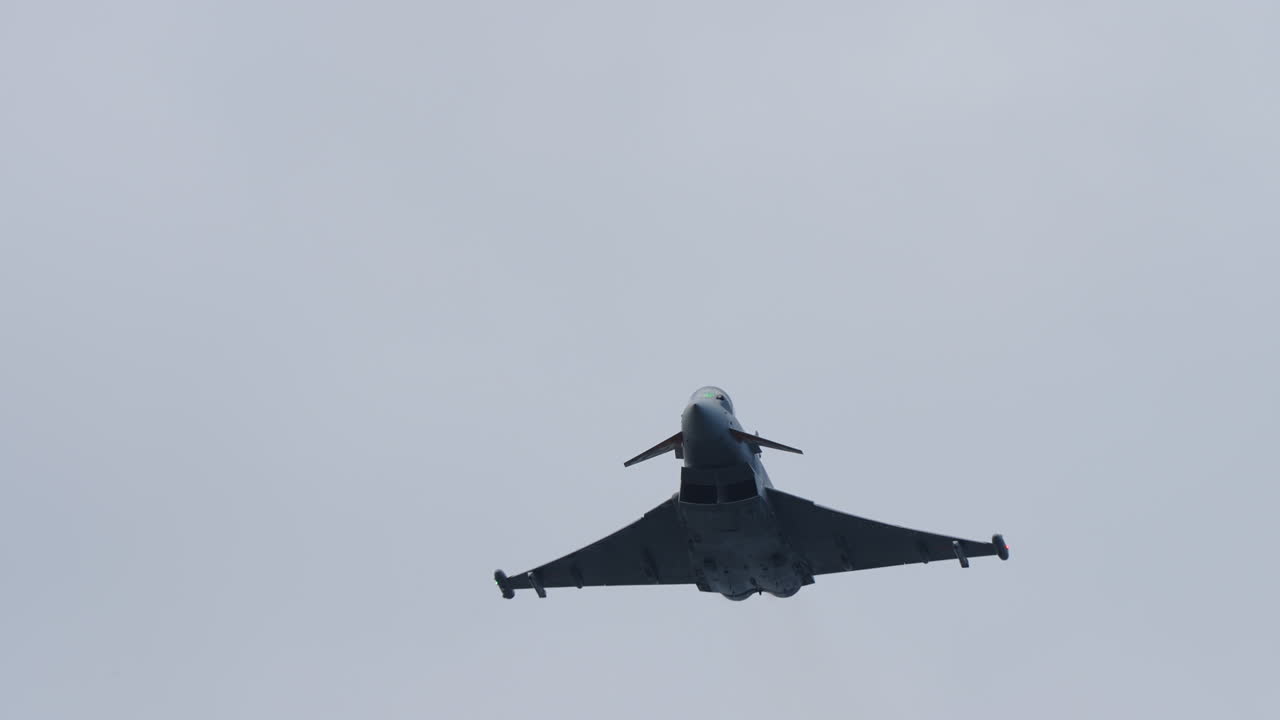 Military jet aircraft flying directly overhead with wide wings and silhouette clearly visible against cloudy sky