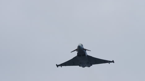 military jet aircraft flying directly overhead with wide wings and silhouette clearly visible against cloudy sky