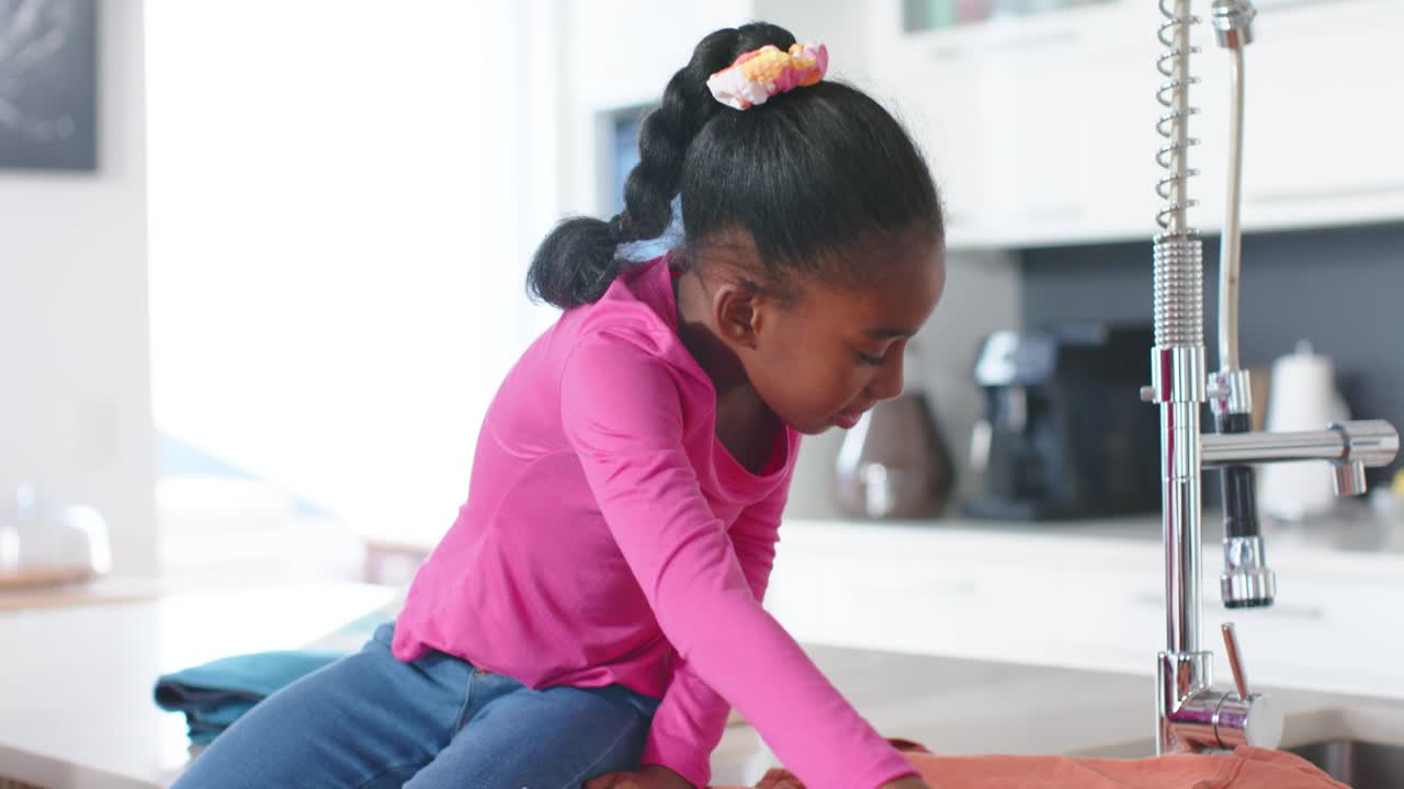African American child seeing wrinkles unfolding and smoothing orange cloth on counter in pink top