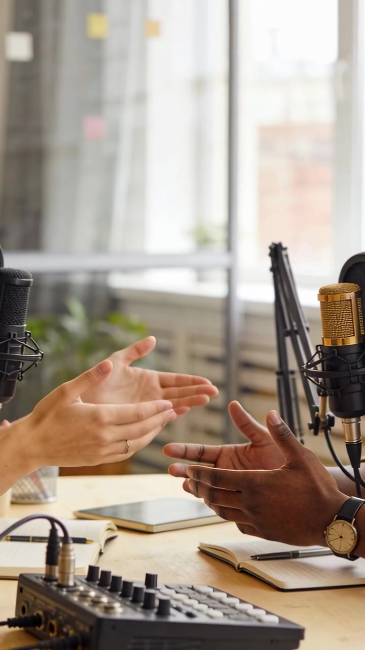 Diversi co-conduttori gesticolano mentre registrano un podcast alla scrivania con microfono dorato e mixer