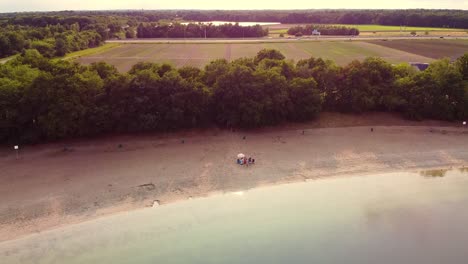 aerial view above a lake beach with multicultural friends hanging out, distant agrilcural fields and highway near breda, netherlands.