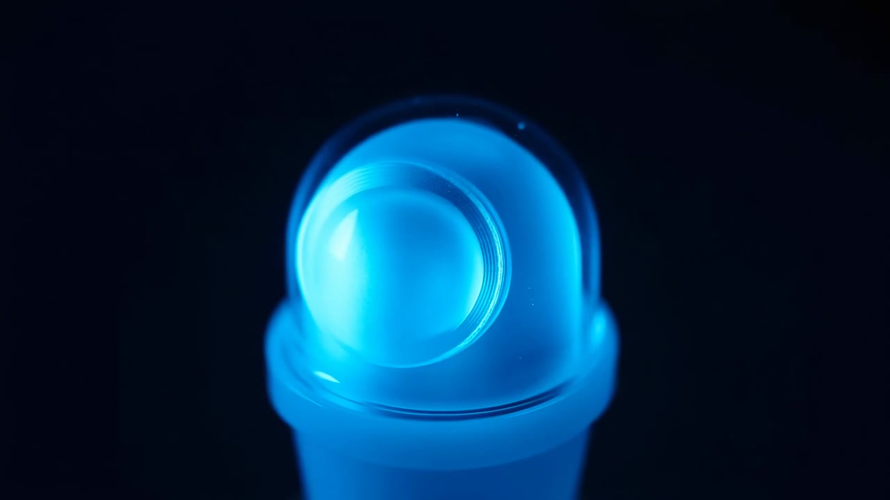 Close view shows a bright cyan-blue translucent form with nested rounded contours and glossy reflections, while subtle changes in light reveal smooth surfaces against deep darkness.