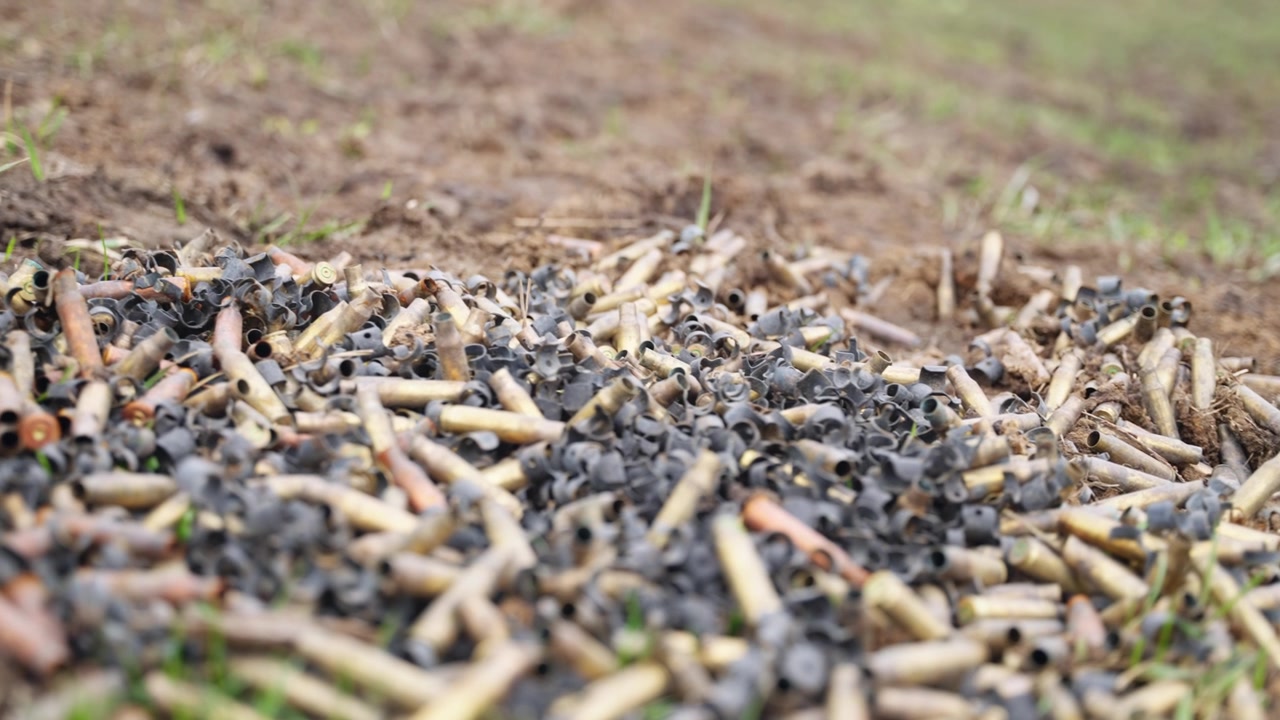 Large pile of spent bullet casings scattered on ground with metallic shells in outdoor setting