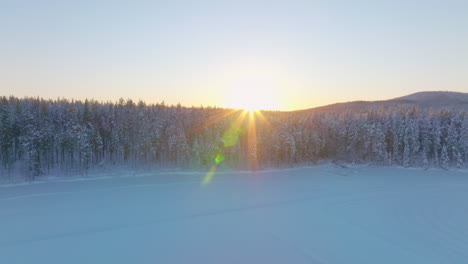 Norbotten-Swedish-Lapland-Polar-circle-aerial-view-glowing-golden-sunrise-above-snow-covered-woodland-and-ice-lake