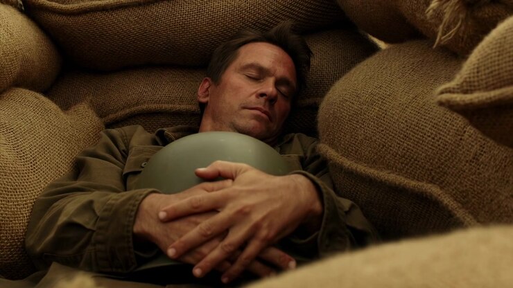 Hands stay clasped around smooth green helmet as reclining man remains still between rough brown sacks, while warm shadows and progressively closer framing reveal woven texture.