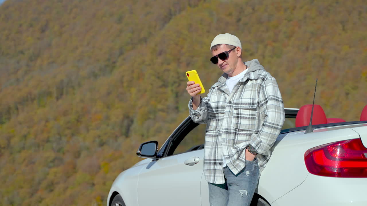 hombre tomando una selfie en un coche convertible por las montañas en otoño