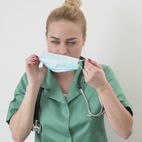 Portrait-of-young-adult-female-doctor-in-green-doctor's-coat-puts-on-a-medical-mask
