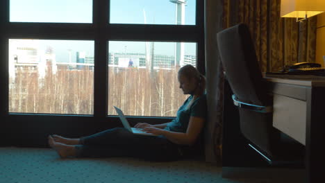 Mujer-Usando-Una-Computadora-Portátil-Junto-A-La-Ventana-En-La-Habitación-Del-Hotel