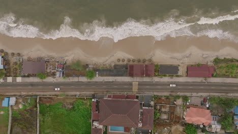 Top-down-aerial-footage-of-a-road-and-beach-and-ocean-waves-just-outside-of-Freetown,-Sierra-Leone